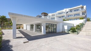 A modern hotel entrance with a covered walkway, glass doors, and a staircase leading to the building. - Sunrise Heights 2455 Sea View (Manilva)