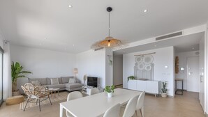 A modern living room with a white sofa, a dining table with chairs, and a hanging light fixture. - Sunrise Heights 2455 Sea View (Manilva)