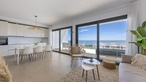 A modern living room with a large window, a dining area, and a kitchen. - Sunrise Heights 2455 Sea View (Manilva)