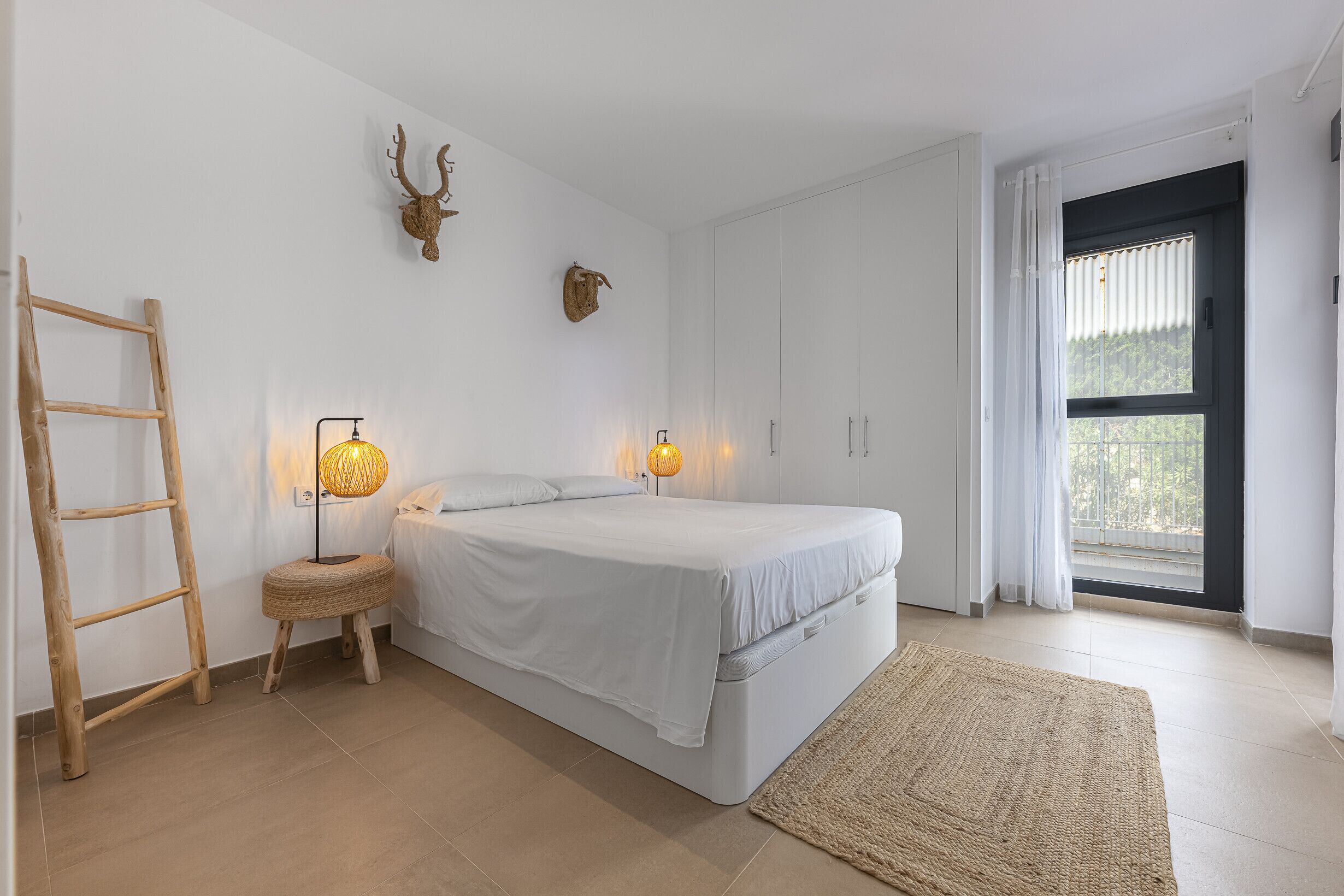 Et soveværelse med seng, stige, lampe og et vindue med gardiner.