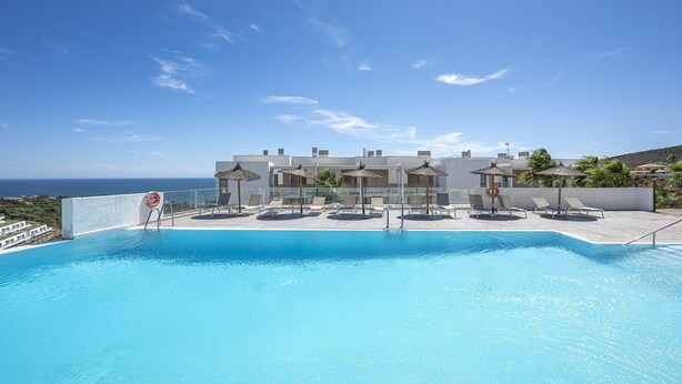 A swimming pool with lounge chairs and umbrellas, overlooking a coastal area. - Sunrise Heights 2455 Sea View (Manilva)