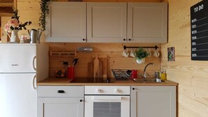 Una cocina funcional con gabinetes blancos, un lavamanos y una estufa. Hay un calendario en la pared y una cesta de frutas sobre la encimera.