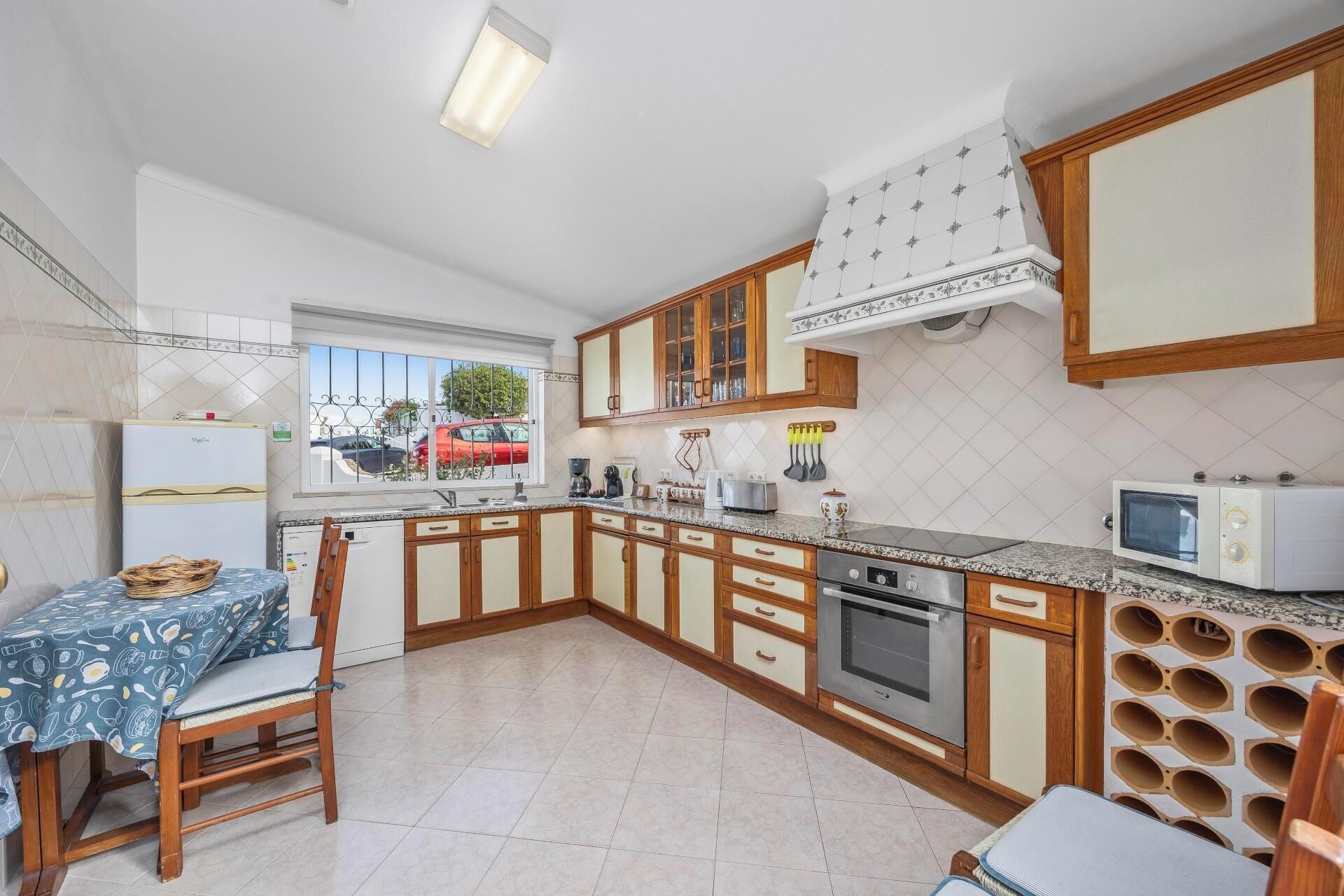 A compact kitchen with a dining area, featuring a refrigerator, stove, microwave, and a window with a view of a red car outside.