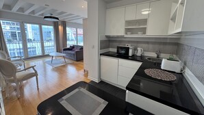 A modern kitchen with a black countertop, white cabinets, and a microwave. There is a dining area with a white table and chairs, and a balcony with a view of the city. - City View Apartments (Belgrade)