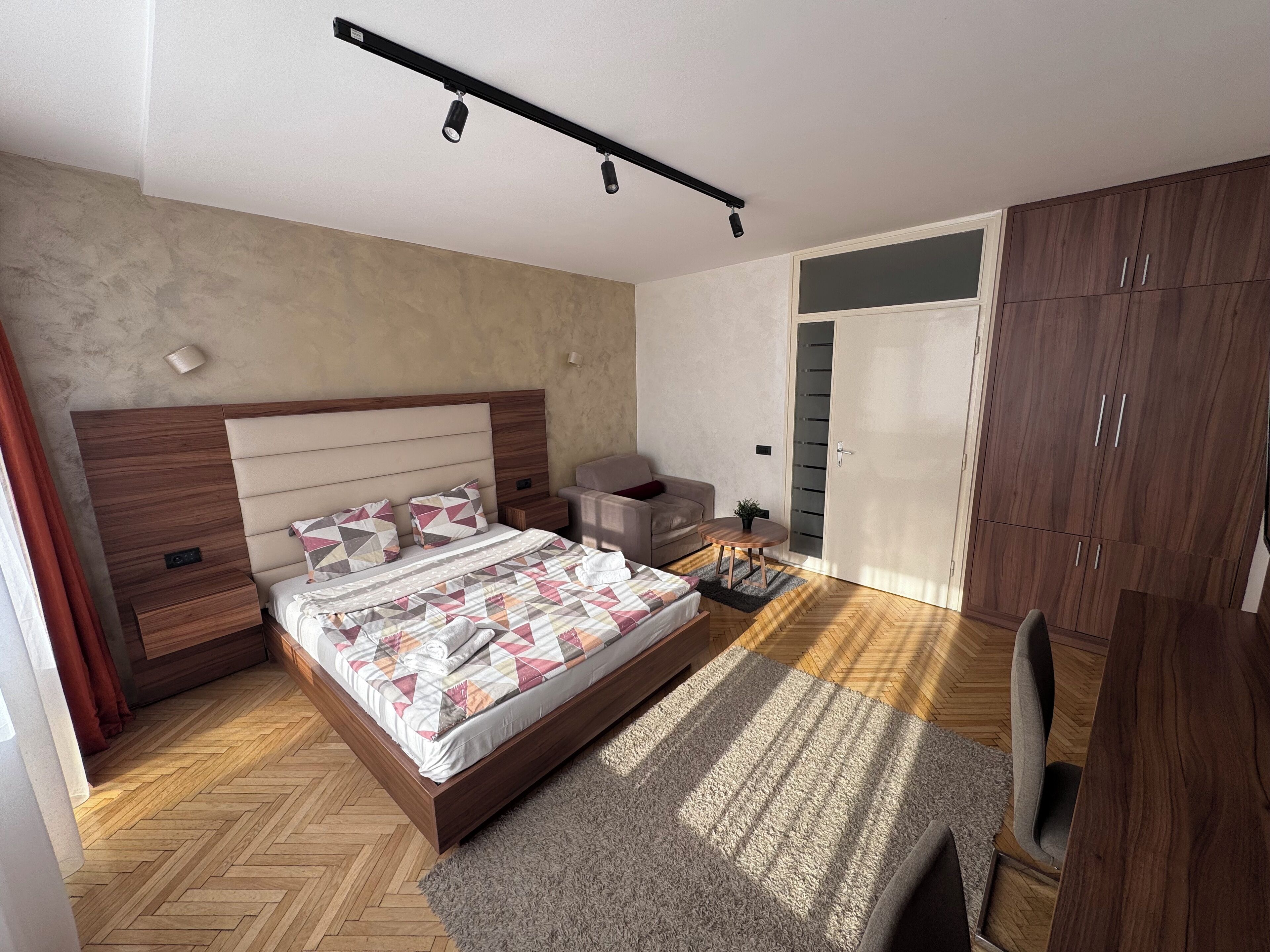 A modern bedroom with a wooden bed, a small sofa, a desk, and a wardrobe.