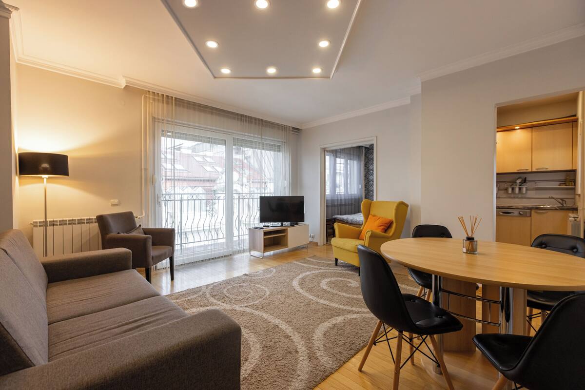 A modern living room with a sofa, chairs, a dining table, and a TV.