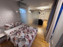 Un dormitorio moderno con una colcha de estampado geométrico, una mesita de noche y vistas a una sala de estar contigua.