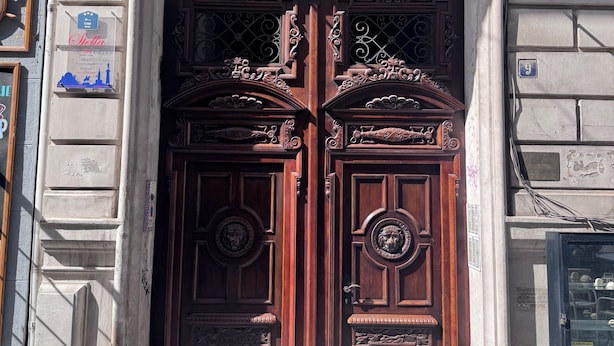 A double wooden door with intricate carvings and a metal gate above it. - City View Apartments (Belgrade)