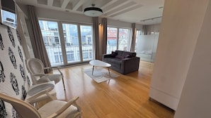 A spacious living room with a sofa, chairs, a coffee table, and large windows offering a view of the city. - City View Apartments (Belgrade)