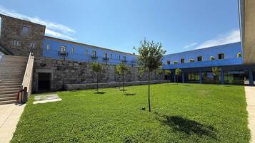 Un patio con un muro de piedra, un edificio azul y un área verde con árboles.