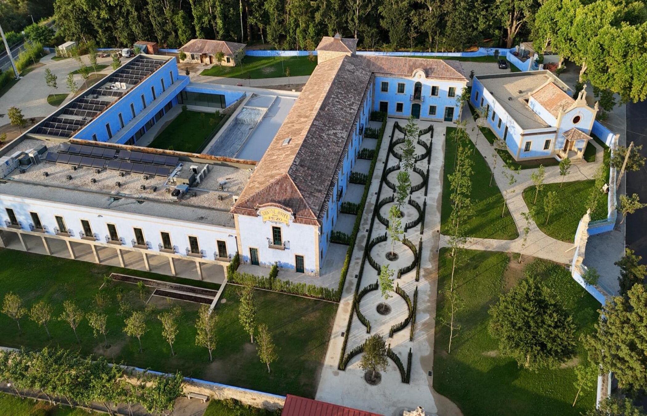 Vista aérea de un edificio grande e histórico con un patio central, rodeado de estructuras más pequeñas y abundante vegetación.