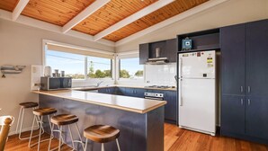 Une cuisine moderne avec un plafond en bois, un îlot central doté de tabourets, un réfrigérateur et une vue sur l’extérieur.