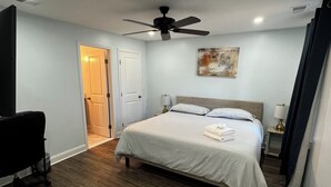 Une chambre à coucher avec un lit, un ventilateur de plafond, un bureau et une porte.