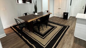 Une cuisine moderne avec une table à manger en bois, des chaises noires, une plante en pot et une poubelle noire.