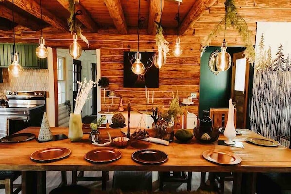 A wooden dining table with plates, a vase, and hanging light fixtures in a rustic interior.