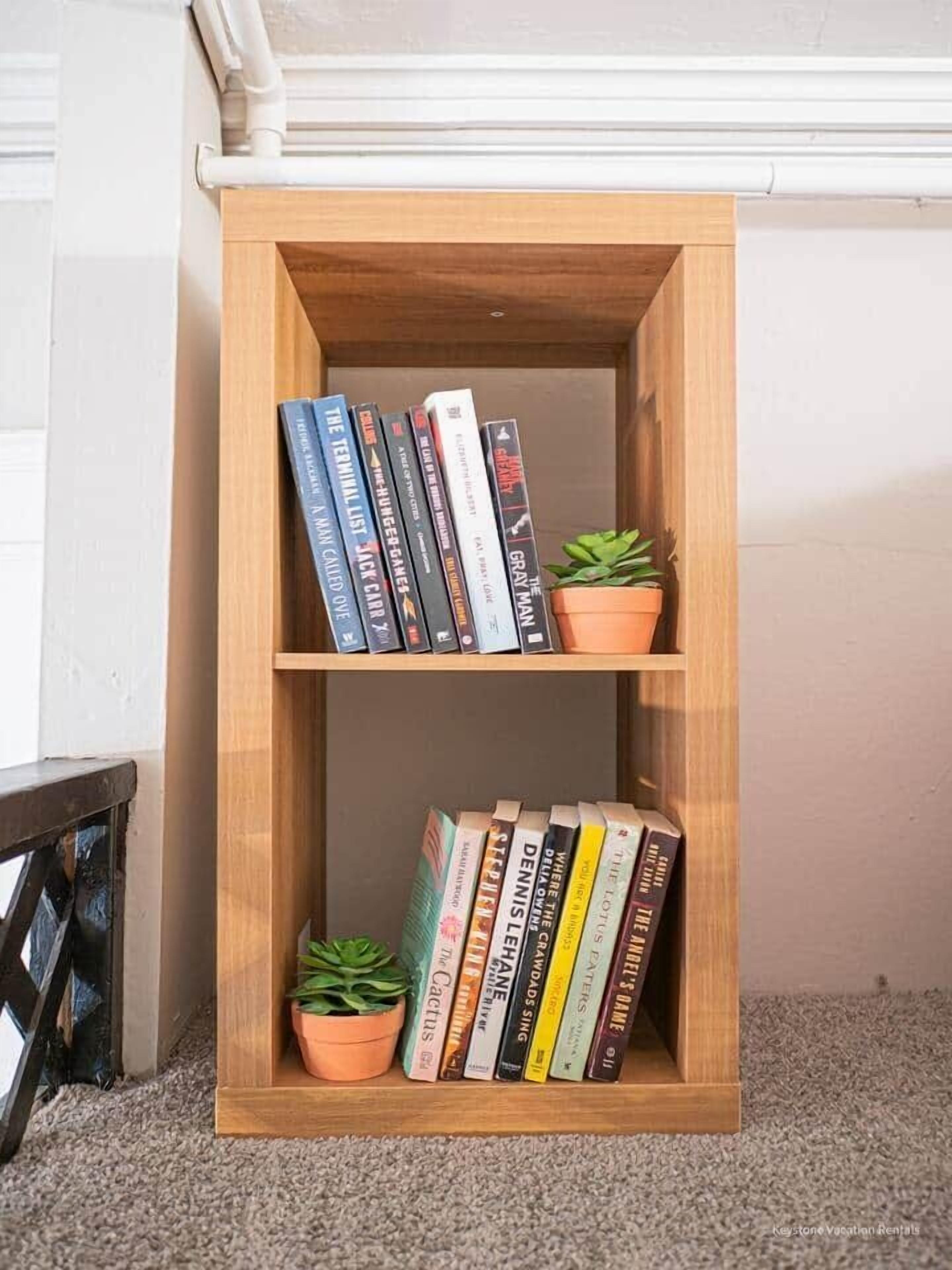 A wooden bookshelf with two shelves, each holding books and small potted plants.