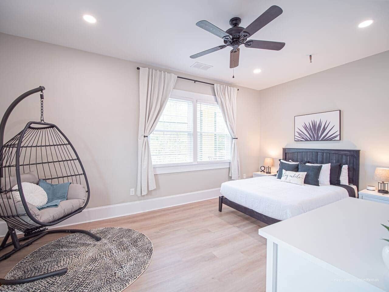 A bedroom with a bed, a hanging chair, a ceiling fan, and a window with curtains.