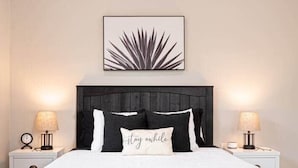 Quarto com uma cama, duas mesas de cabeceira, uma obra de arte na parede e um abajur.