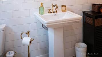 A bathroom with a white pedestal sink, a framed mirror, and a wall with a floral wallpaper pattern.