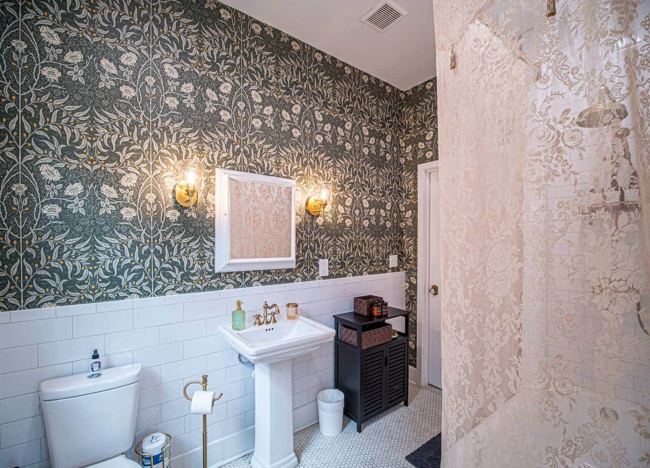 A bathroom with a white toilet, a pedestal sink, and a black vanity with a mirror. There are two wall sconces with light bulbs.