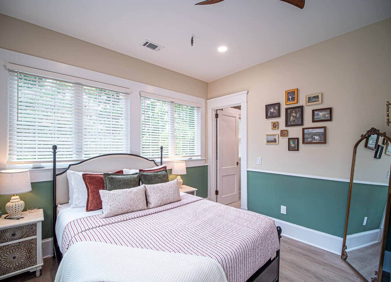 A bedroom with a bed, bedside tables, a nightstand, a mirror, a dresser, a wardrobe, a ceiling fan, and a window with blinds.