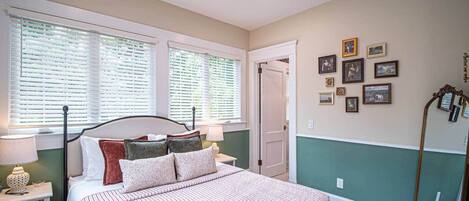 A bedroom with a bed, bedside tables, a nightstand, a mirror, a dresser, a wardrobe, a ceiling fan, and a window with blinds.