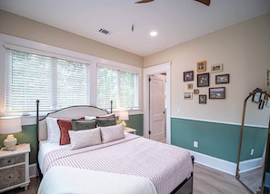 A bedroom with a bed, bedside tables, a nightstand, a mirror, a dresser, a wardrobe, a ceiling fan, and a window with blinds. - The Marietta Square Manor (Marietta)