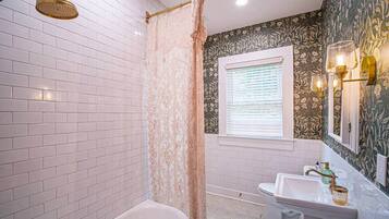 A bathroom with a white bathtub, a shower with a gold showerhead, a sink with a gold faucet, and a window with blinds.