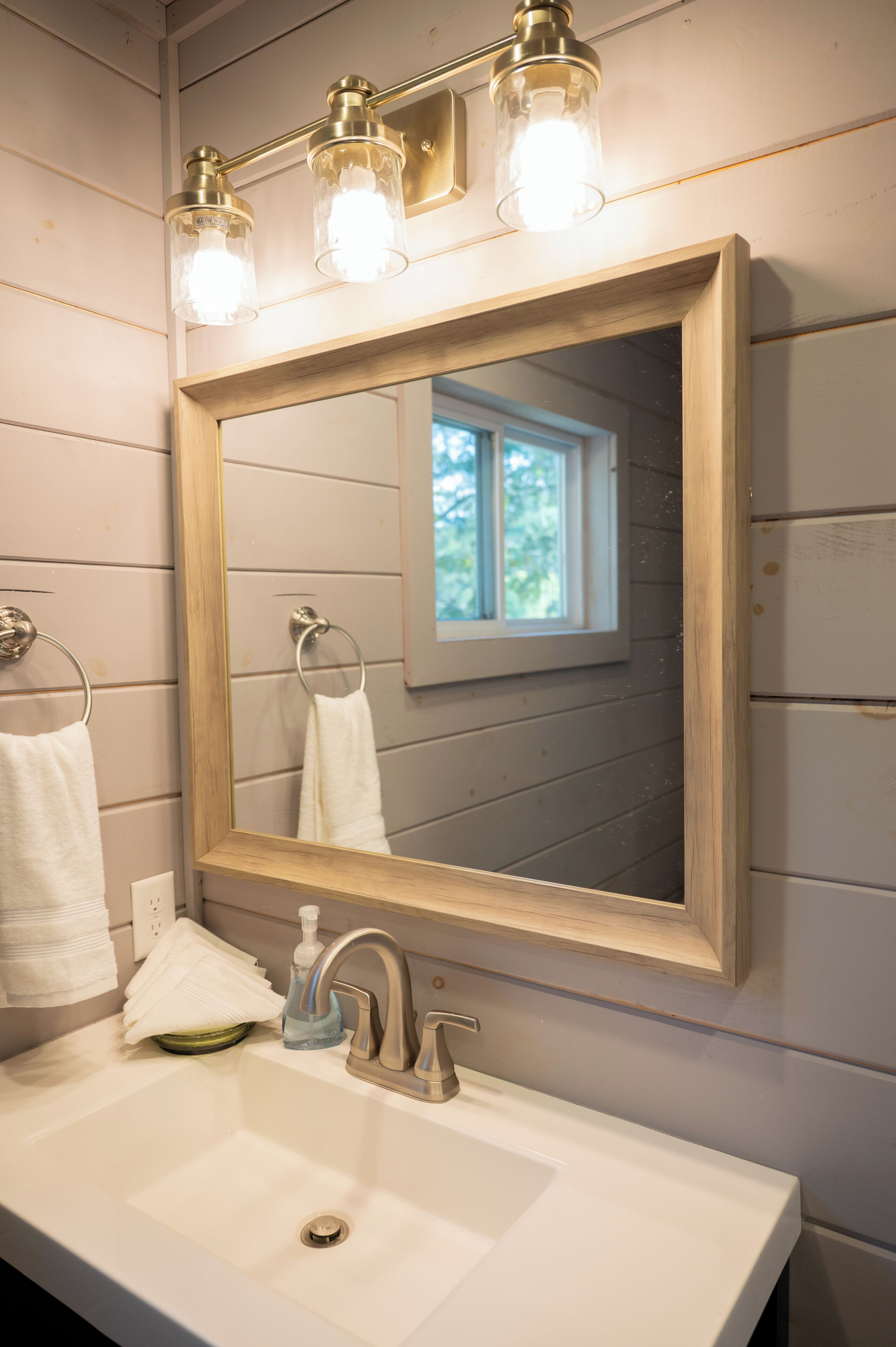 A bathroom with a wooden-framed mirror, a white sink, and a window above the mirror.