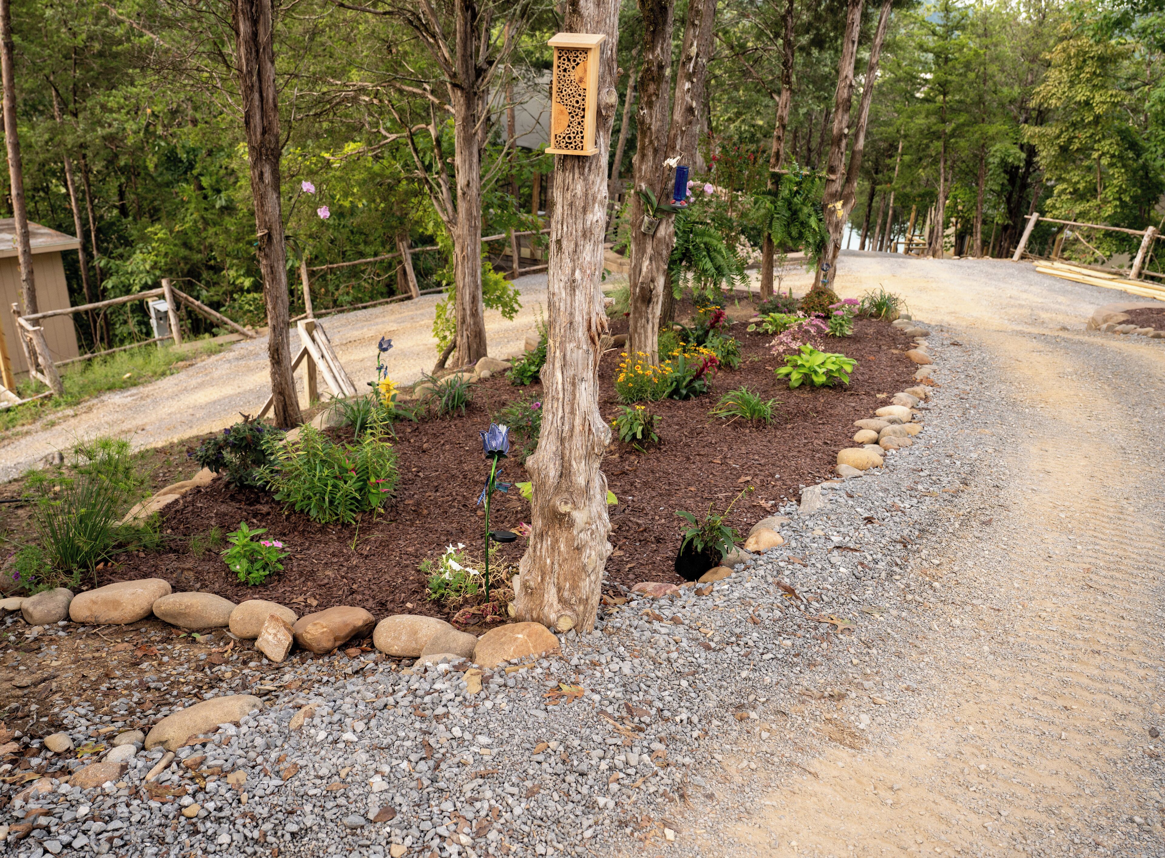 Un jardín con un camino de grava, diversas plantas y una estructura de madera.