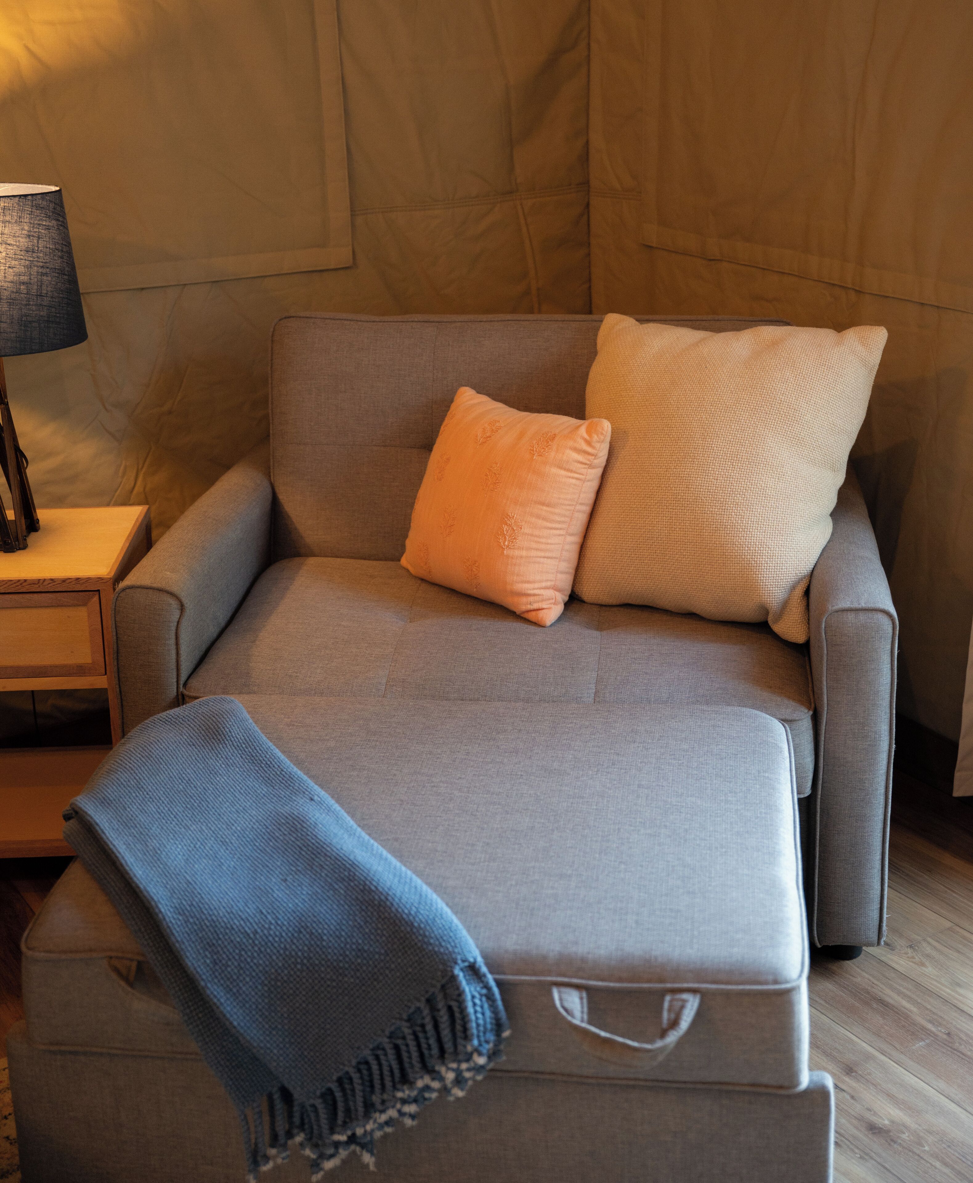 Een moderne bank met twee kussens en een plaid, geplaatst tegen een houten wand.