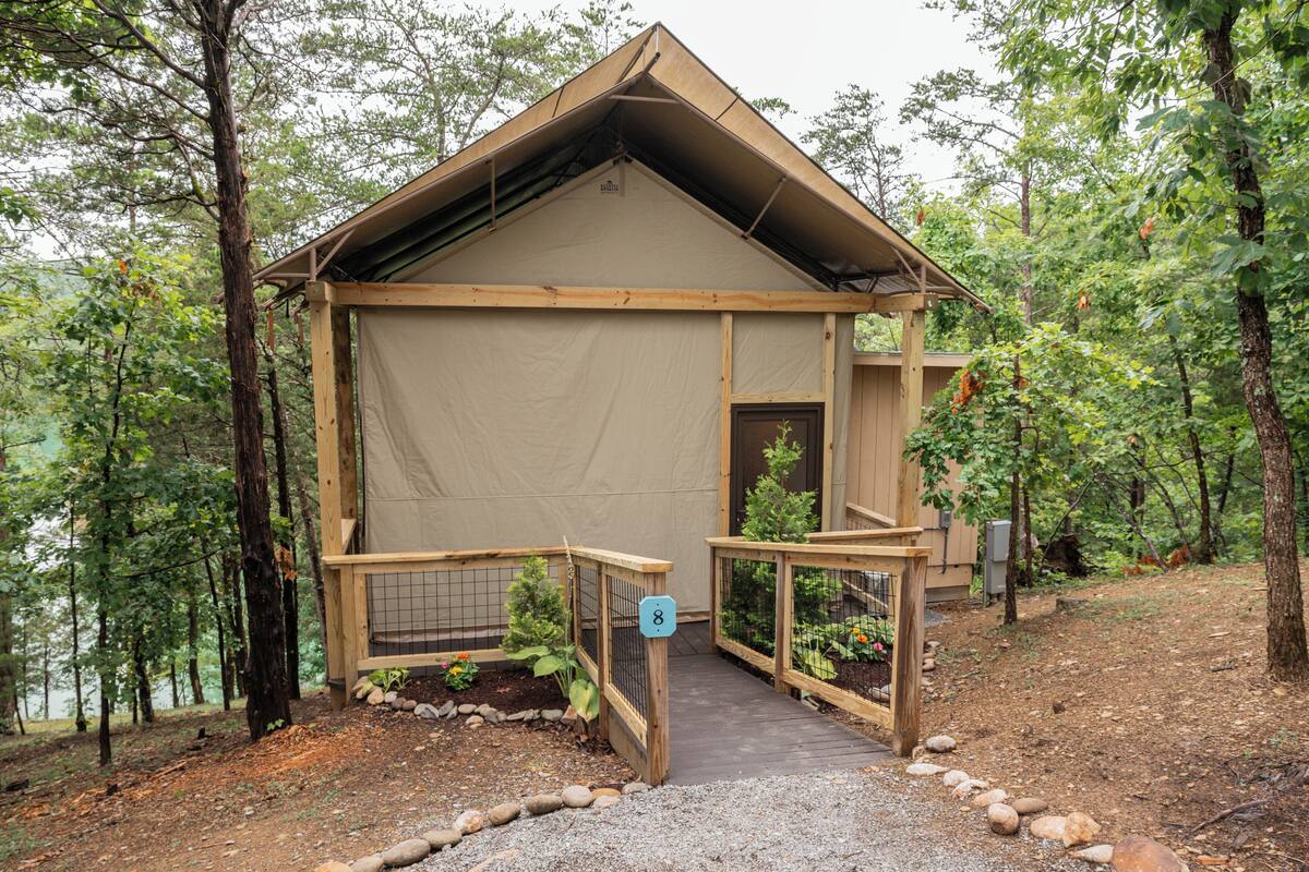 A small, single-story cabin with a sloped roof, a wooden deck, and a fenced garden area.