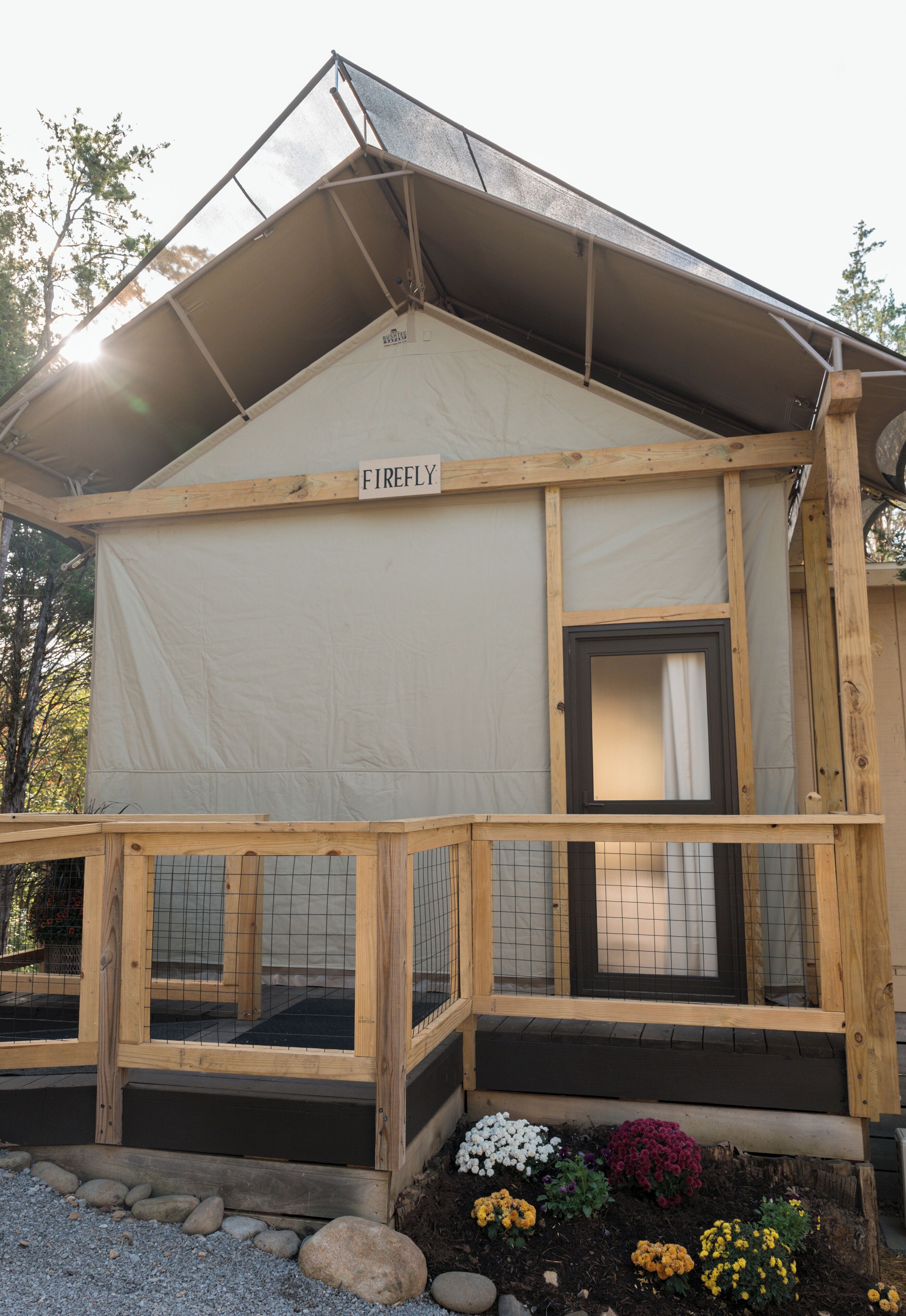 Une cabane en bois avec une enseigne représentant une luciole, un porche couvert et un jardin où poussent différentes sortes de fleurs.