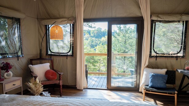 A bedroom with a large bed, a wooden chair, a small table, and a window with a view of trees. - WYLDSTAY Smoky Mountains (Sevierville)