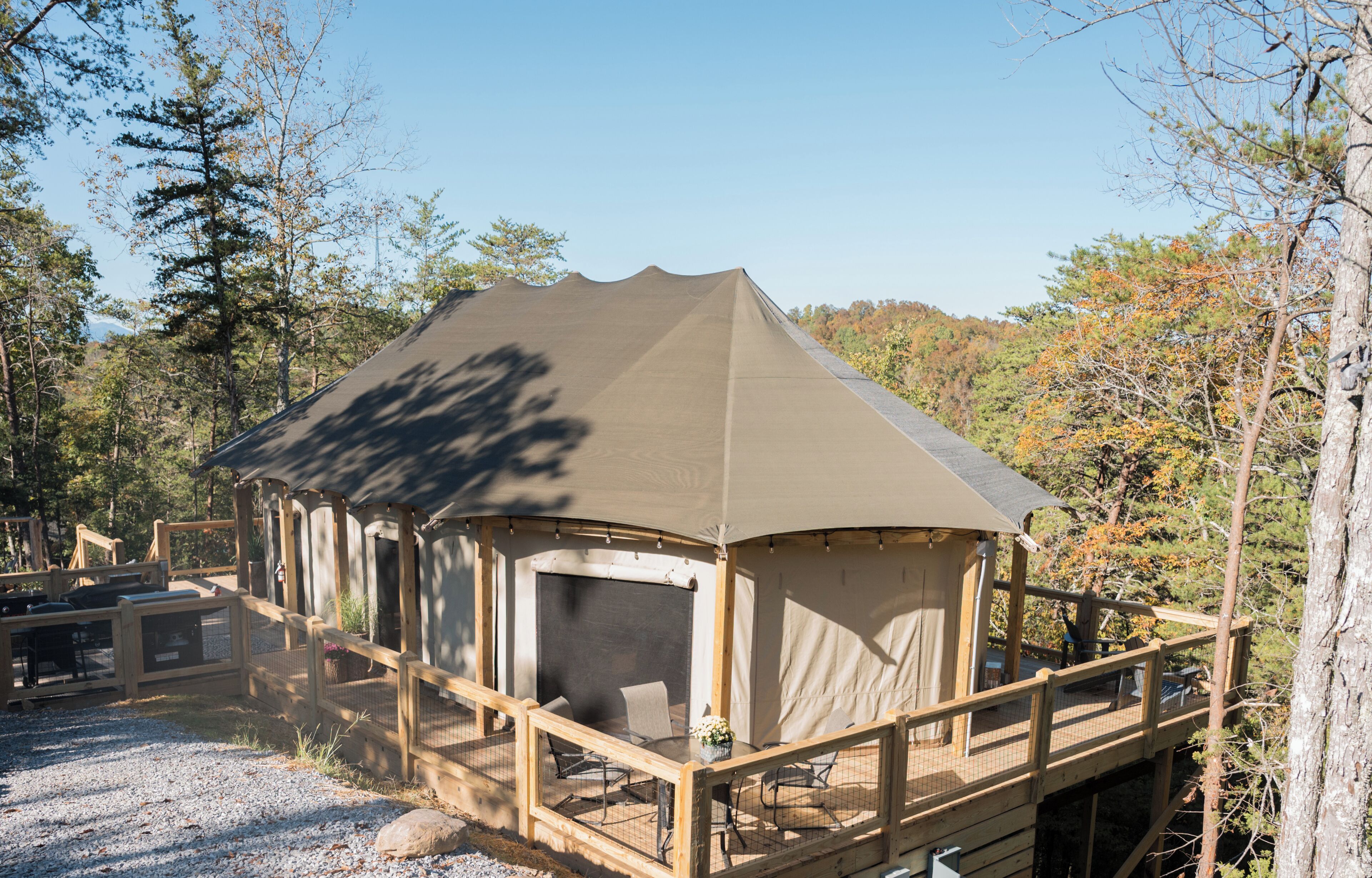 A wooden cabin with a covered porch, a dining area, and a view of the surrounding forest.