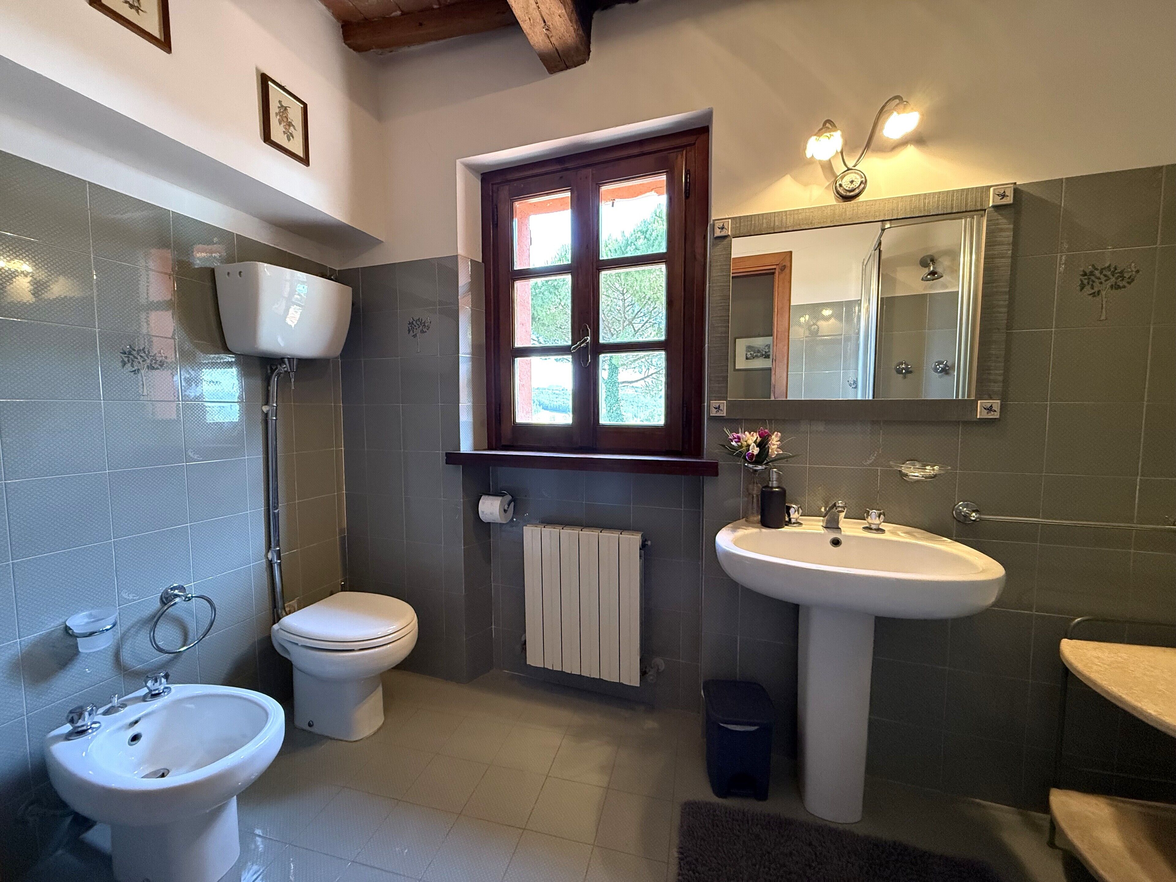 Et badeværelse med toilet, bidet, vask og vindue.