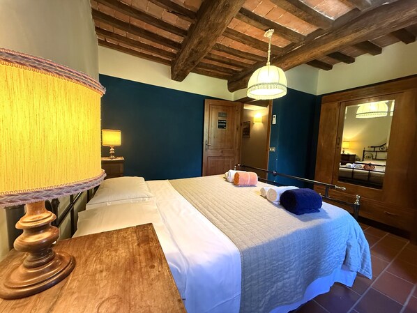A hotel room with a wooden ceiling, a bed with white linens, a bedside lamp, and a mirror reflecting the room.