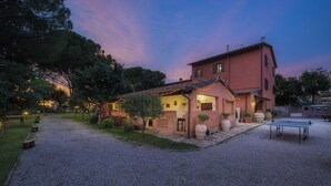 Ein rustikales Haus mit Kiesweg, einer kleinen Terrasse mit Tisch und Stühlen sowie einem Tennisplatz.