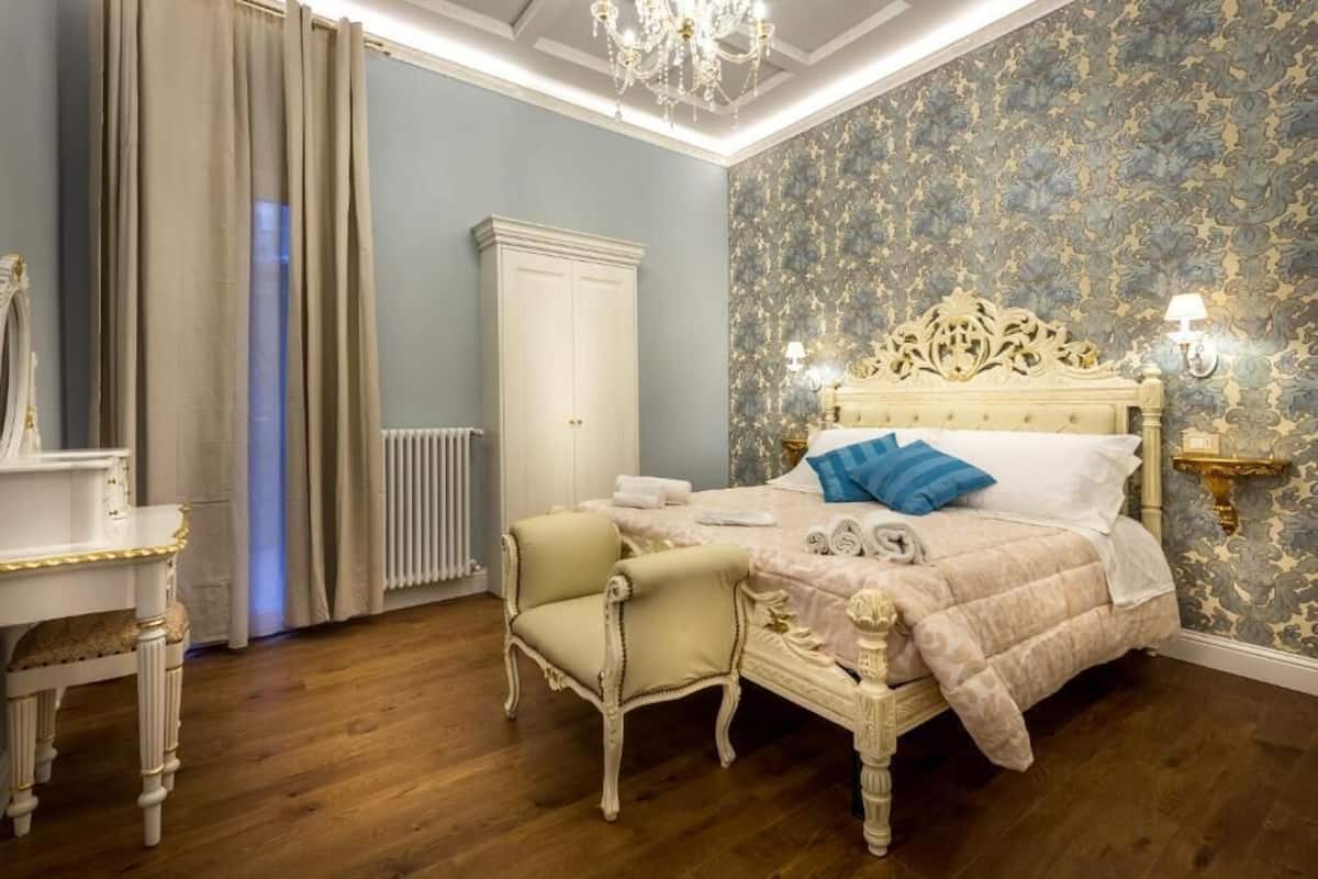 A bedroom with a large bed, a white wardrobe, a small chair, and a chandelier.