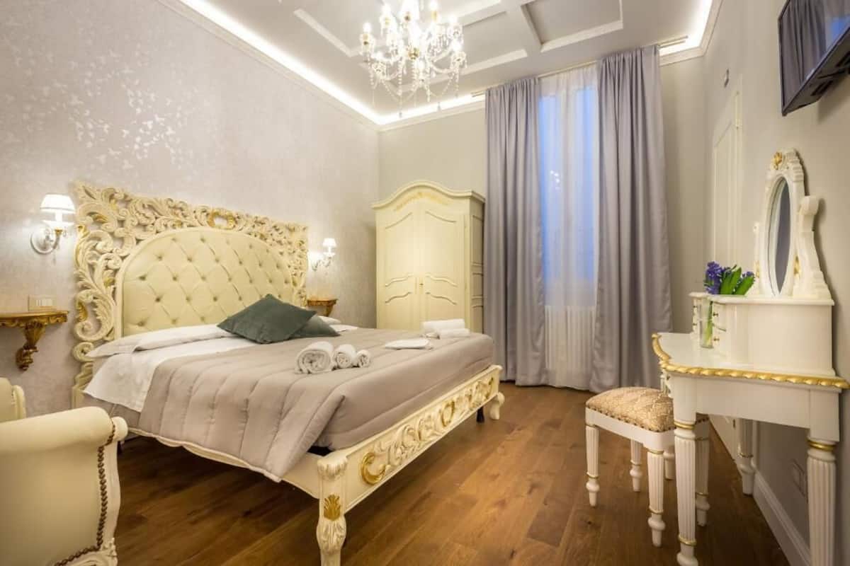 A bedroom with a tufted headboard, a bedside table with a lamp, a dresser, and a chair.