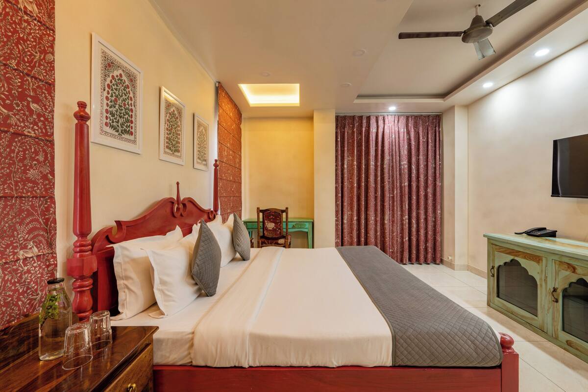 A well-lit bedroom with a large bed, a wooden nightstand, a television, and a ceiling fan.