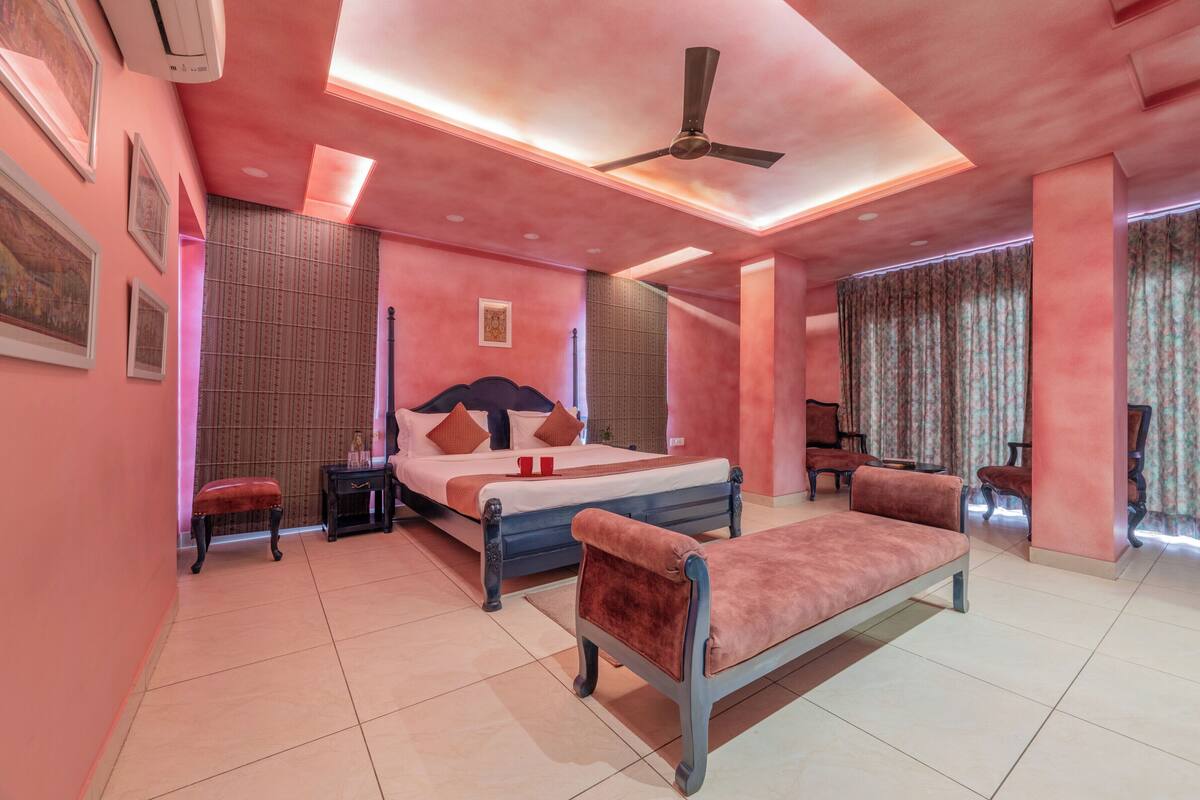A pink-themed bedroom with a bed, a bench, a ceiling fan, and a window with curtains.