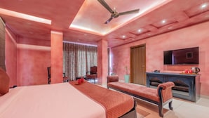 A bedroom with a large bed, a seating area, a TV, and a desk with a coffee maker. - Baari the house fusion (Jaipur)