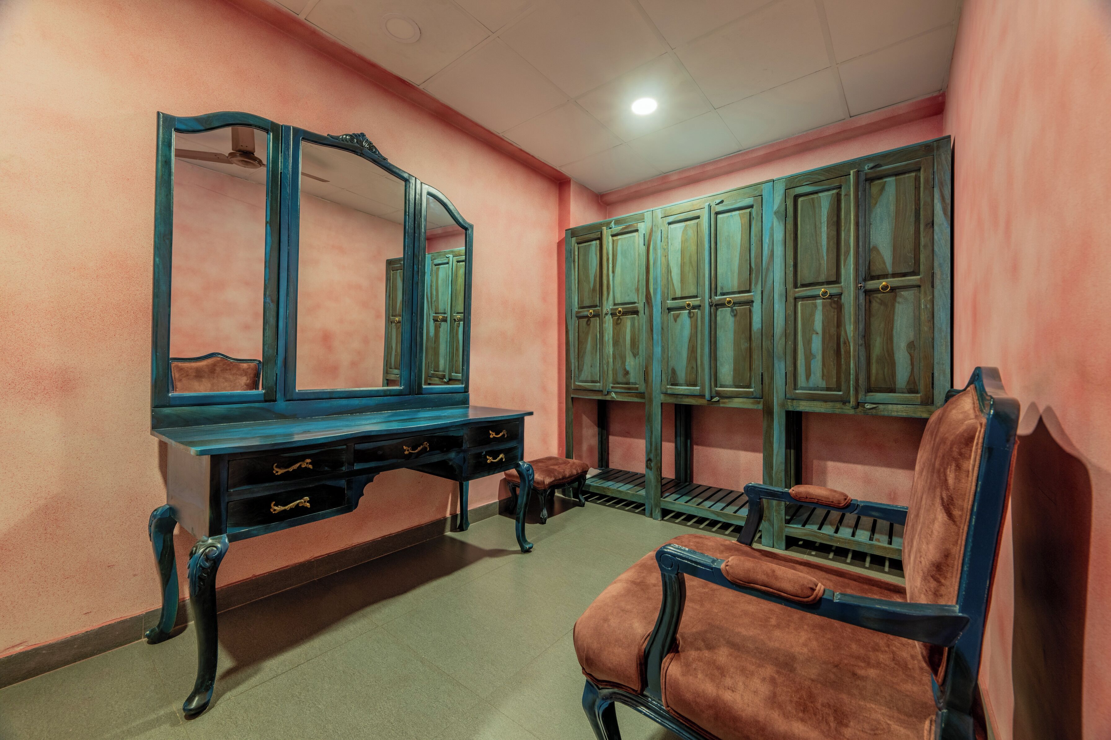 A room with a vanity, a mirror, a bench, and wooden cabinets.