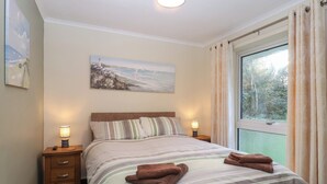 A bedroom with a bed, two bedside tables, a painting, and a window with curtains. - Willow Lodge (Liskeard)