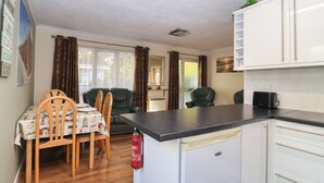 A compact kitchen with white cabinets, a black countertop, and a dining area with a table and chairs. - Willow Lodge (Liskeard)