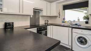 A modern kitchen with white cabinets, a black countertop, a built-in oven, a sink, and a washing machine. - Willow Lodge (Liskeard)