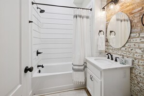 Une salle de bain avec une baignoire blanche, un lavabo blanc et un miroir adossé à un mur en bois.