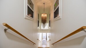 Un escalier avec des rampes en bois, un tapis à motifs au bas de l’escalier et un luminaire suspendu.