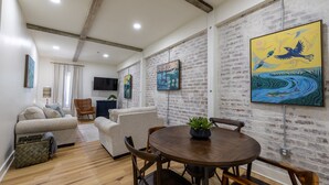 A modern living room with a brick wall, a round wooden dining table, and two sofas. - Adam Trest Suite, Laurel, Coffee Bar, Walkable (Laurel)